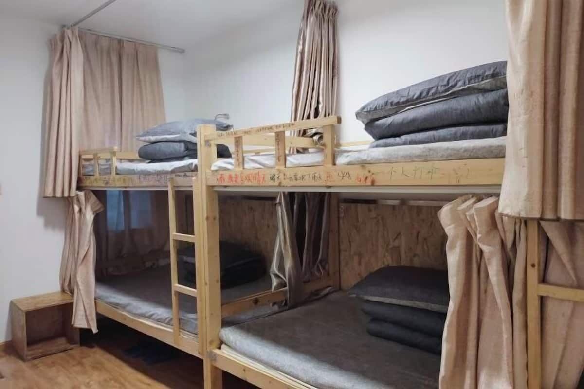 Une chambre avec un lit superposé, des rideaux, une échelle et un petit tabouret en bois.