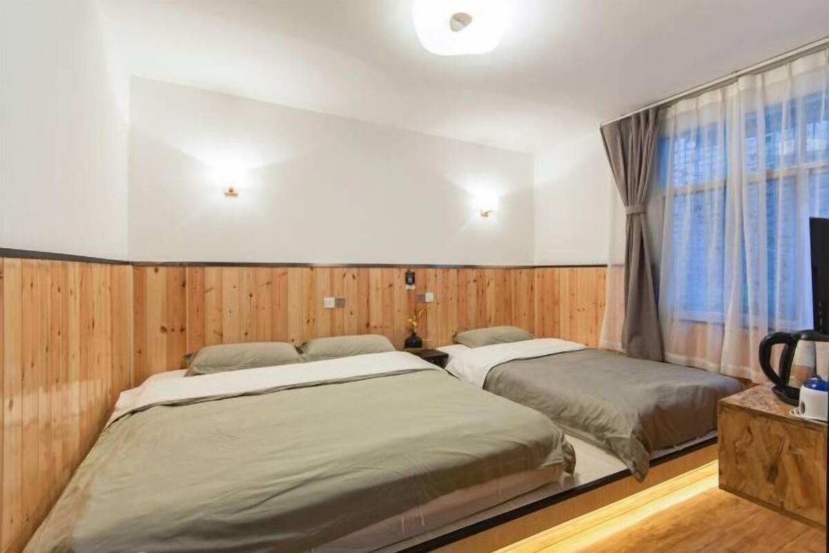 Une chambre d’hôtel avec deux lits, des lambris en bois aux murs, un téléviseur à écran plat, une machine à café et une fenêtre avec des rideaux légers.