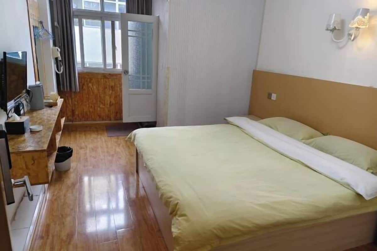 Une chambre d’hôtel avec un lit, un bureau avec un ordinateur, une chaise, une fenêtre avec des rideaux et une porte.