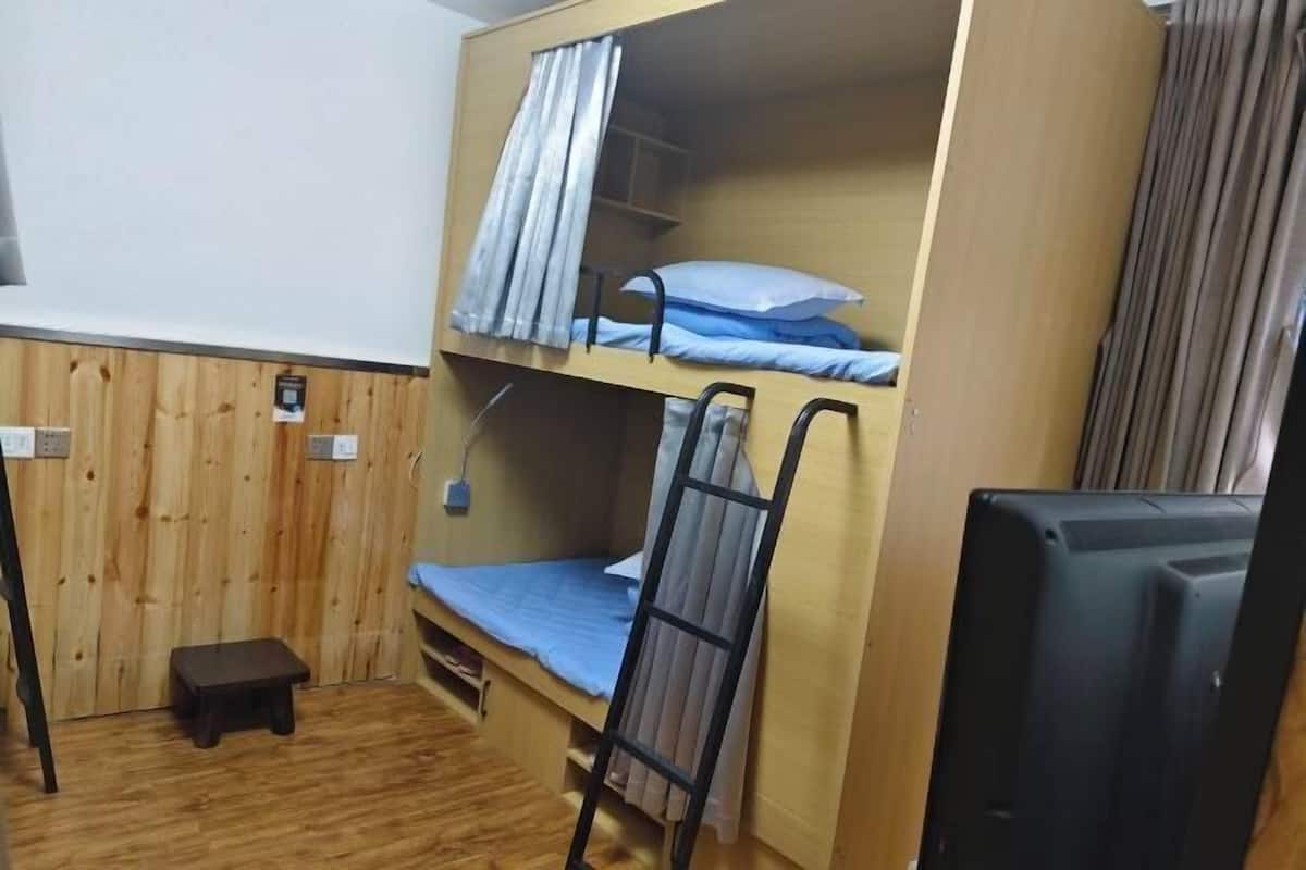 Une chambre avec un lit superposé, un petit tabouret, une échelle et un téléviseur.