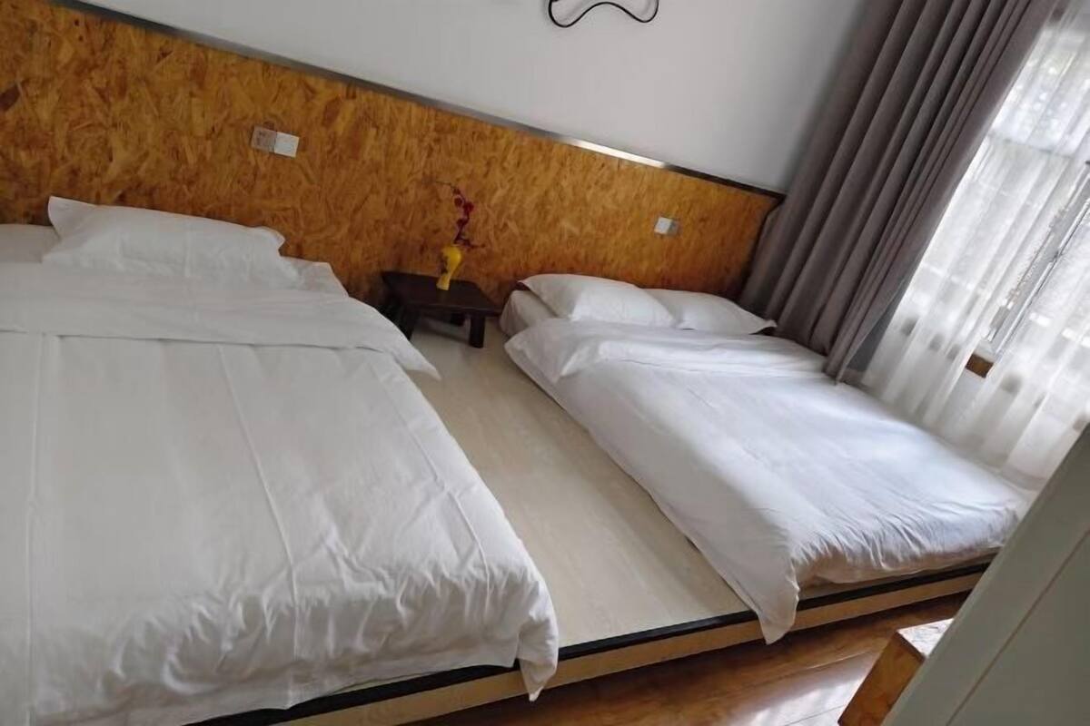 Une chambre d’hôtel avec deux lits simples, une tête de lit en bois, une petite table avec un vase et une fenêtre avec des rideaux.