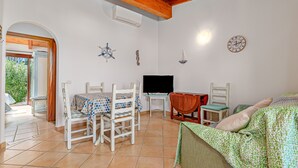 A room with a dining table, chairs, a TV, a bed, and a clock on the wall. - Apartment 'Con Vista Porto Taverna' with Sea View, Private Terrace and Air Conditioning (Monte Petrosu)