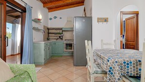 A compact kitchen with a refrigerator, stove, and cabinets. There is a dining area with a table and chairs. - Apartment 'Con Vista Porto Taverna' with Sea View, Private Terrace and Air Conditioning (Monte Petrosu)