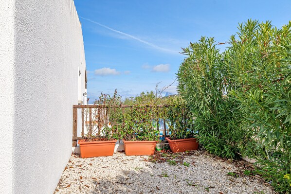 A white building with a gravel patio, potted plants, and a wooden fence.