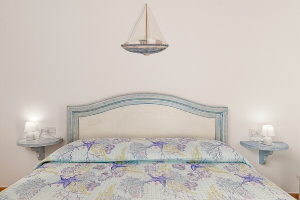 Una cama con colcha estampada, una lámpara colgante y mesitas de noche con lámparas.
