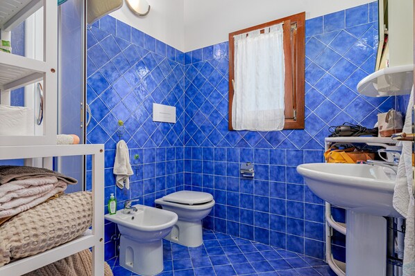 A bathroom with blue tiles, a white sink, a toilet, and a bidet.