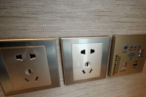 Three electrical outlets on a textured wall, with a control panel featuring a power button and USB port. - Shangyijia Themed Hostel (Yantai)