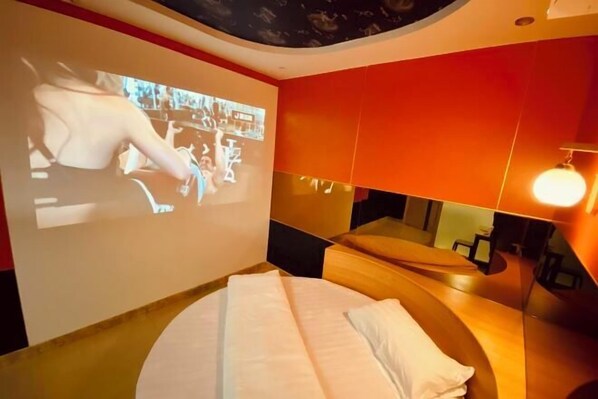 Una habitación de hotel moderna con una cama, una pantalla grande mostrando una película y un diseño de techo único.