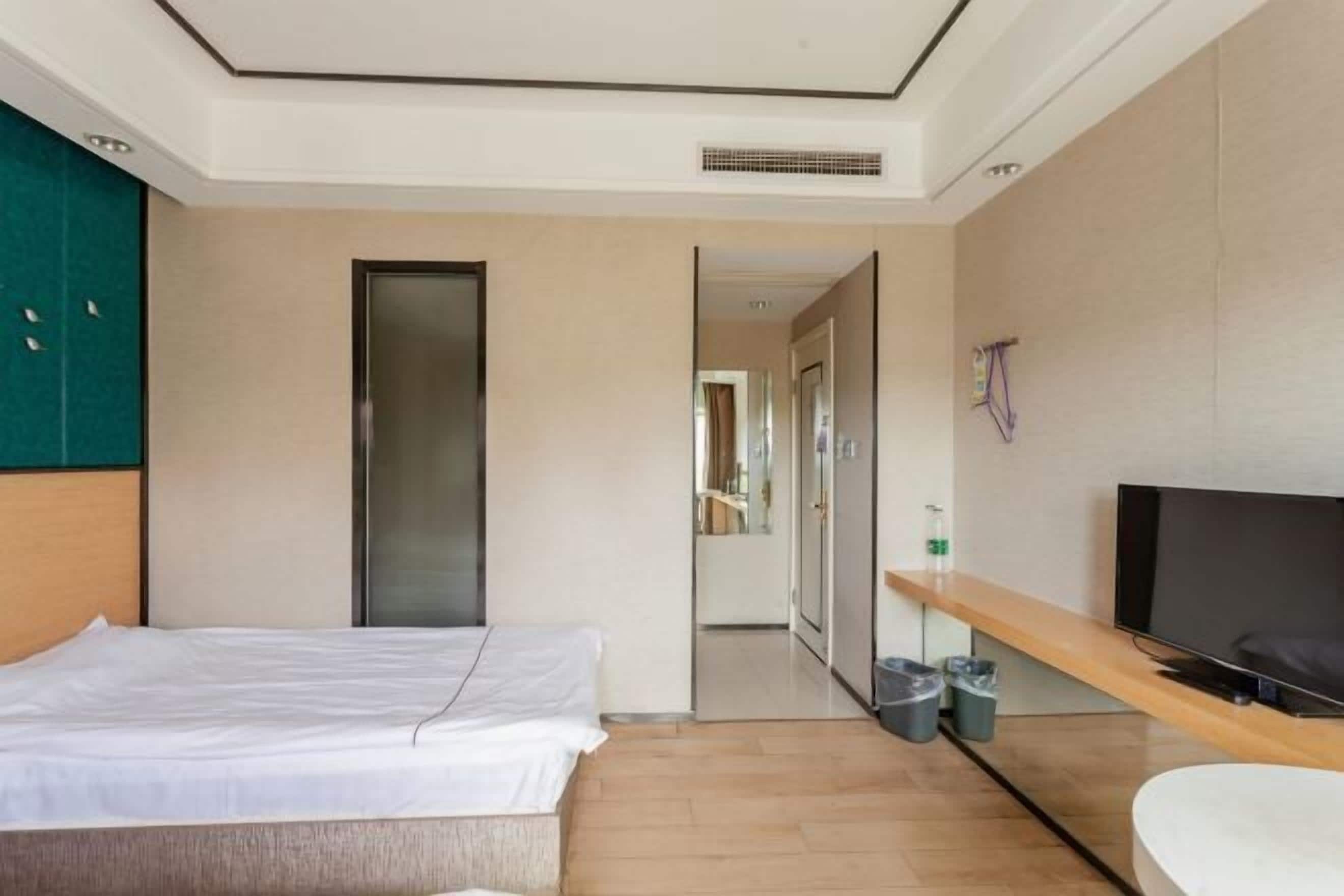 A hotel room with a bed, a TV, a desk, and a bathroom visible through an open door.