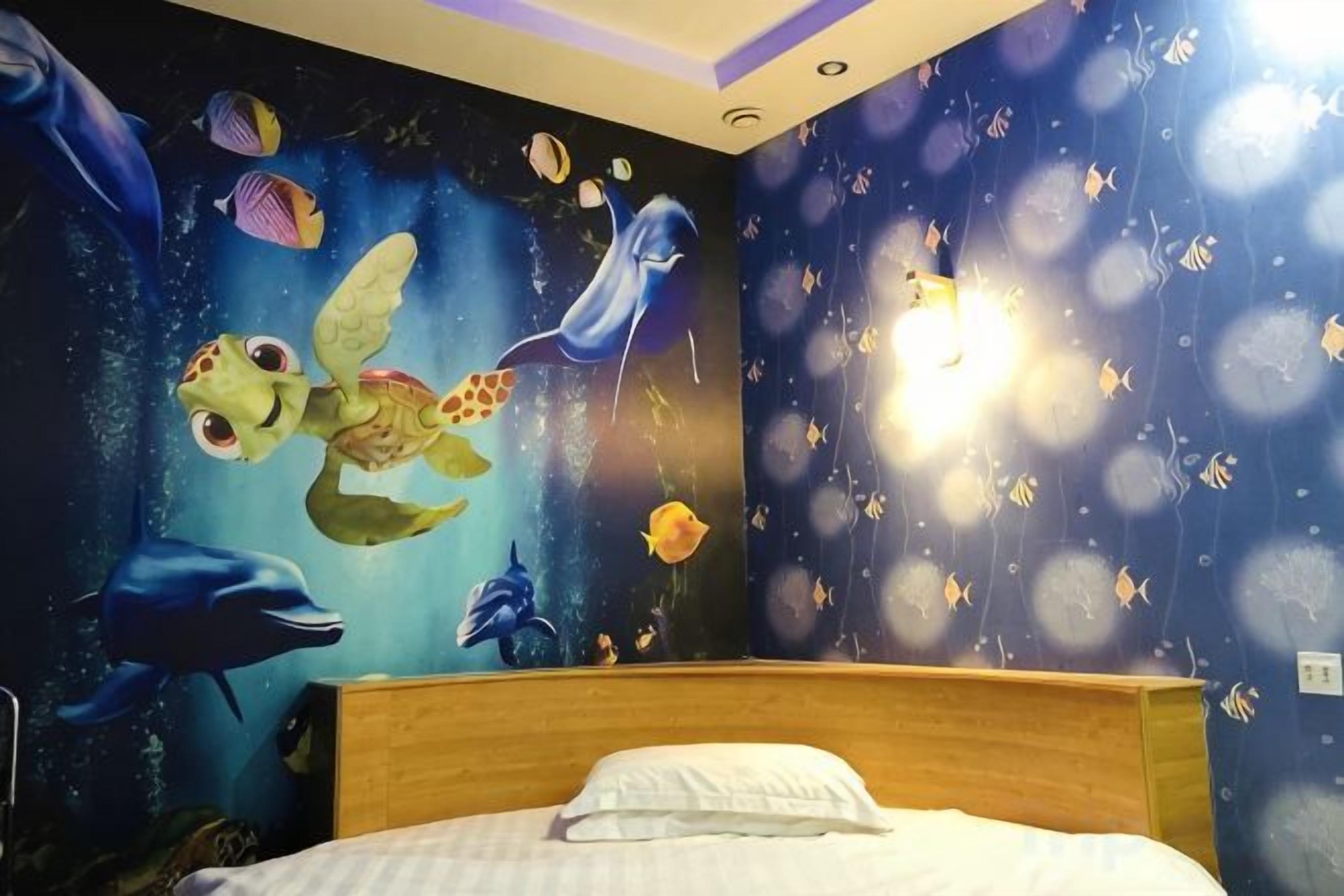 Un dormitorio con un mural de criaturas marinas en la pared, una cama con almohada blanca y cabecera de madera.