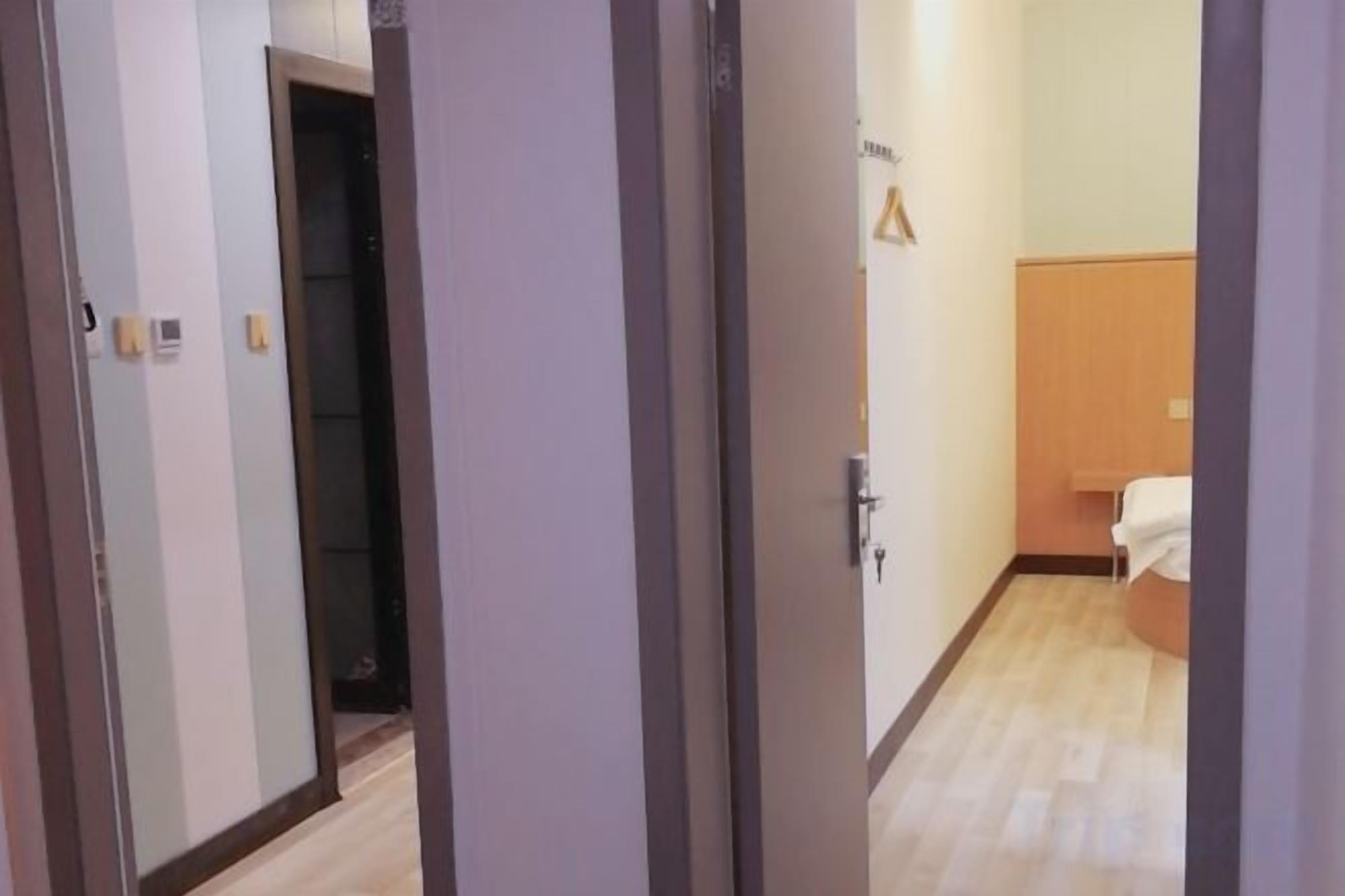 A hallway with a door leading to a room with a bed and a small table.