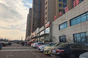 A parking lot with multiple cars, a building with signage, and tall residential buildings in the background. - Shangyijia Themed Hostel (Yantai)