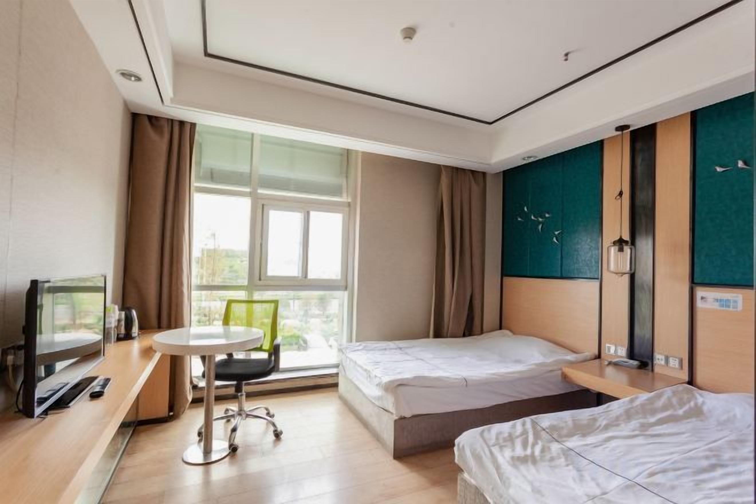 Una camera d'albergo con un letto, un tavolino, una sedia, una televisione e una finestra con tende.