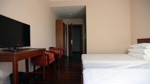 A hotel room with a TV, a desk, two beds, and a hallway leading to another room. - Sanzao Hostel (Shanghai)