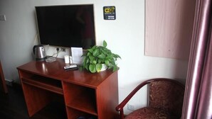A wooden desk with a television, a kettle, a plant, and a remote control. - Sanzao Hostel (Shanghai)