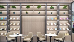 Een modern interieur met meerdere planken waarop boeken en kleine potplanten staan. In het midden staan drie ronde tafels met stoelen.