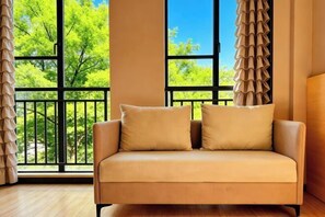 A beige sofa with two cushions in front of a large window with a view of green trees.
