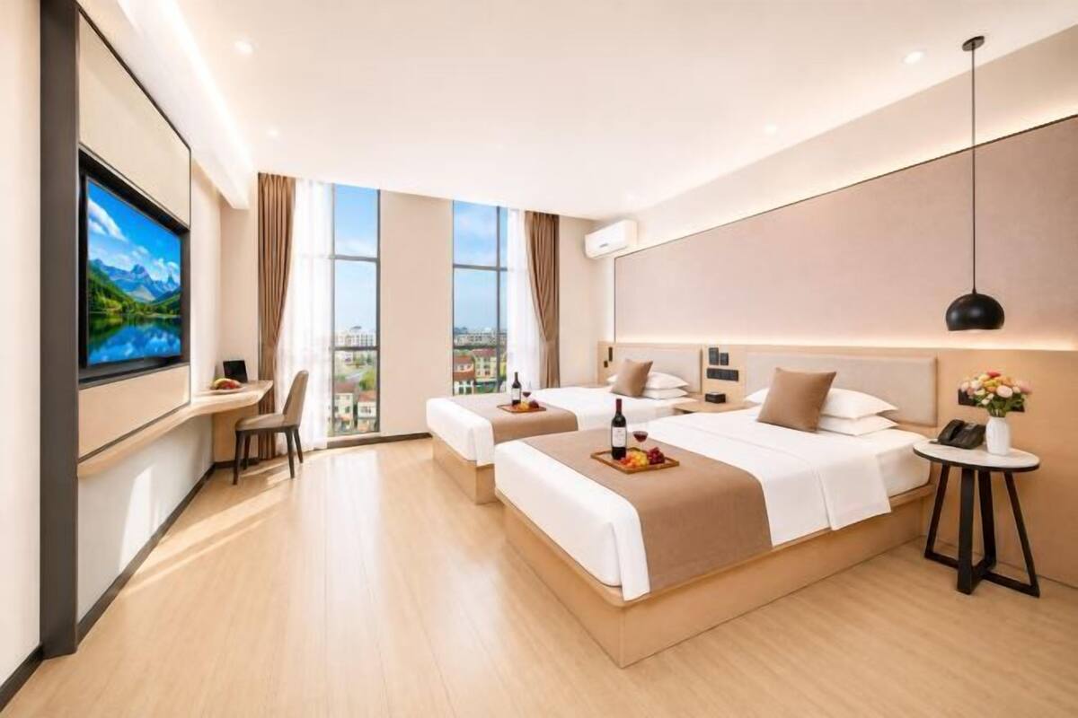 Ein modernes Hotelzimmer mit zwei Betten, einem Fernseher, einem Schreibtisch und Blick auf die Stadt.
