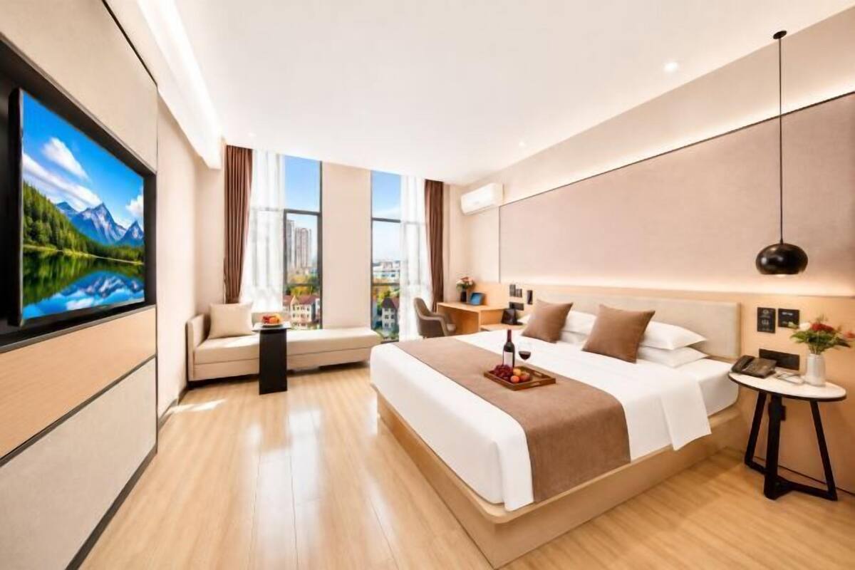 Ein modernes Hotelzimmer mit einem großen Bett, einem Fernseher, einer Couch, einem kleinen Tisch und Blick auf die Stadt.