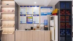 Een receptiegebied van een hotel met een balie, informatieposters, een koffieapparaat, een waterdispenser en een koelkast gevuld met drankjes.