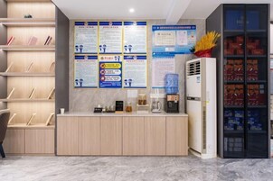 Zona de recepción de un hotel, con mostrador, carteles informativos, máquina de café, dispensador de agua y nevera con bebidas.