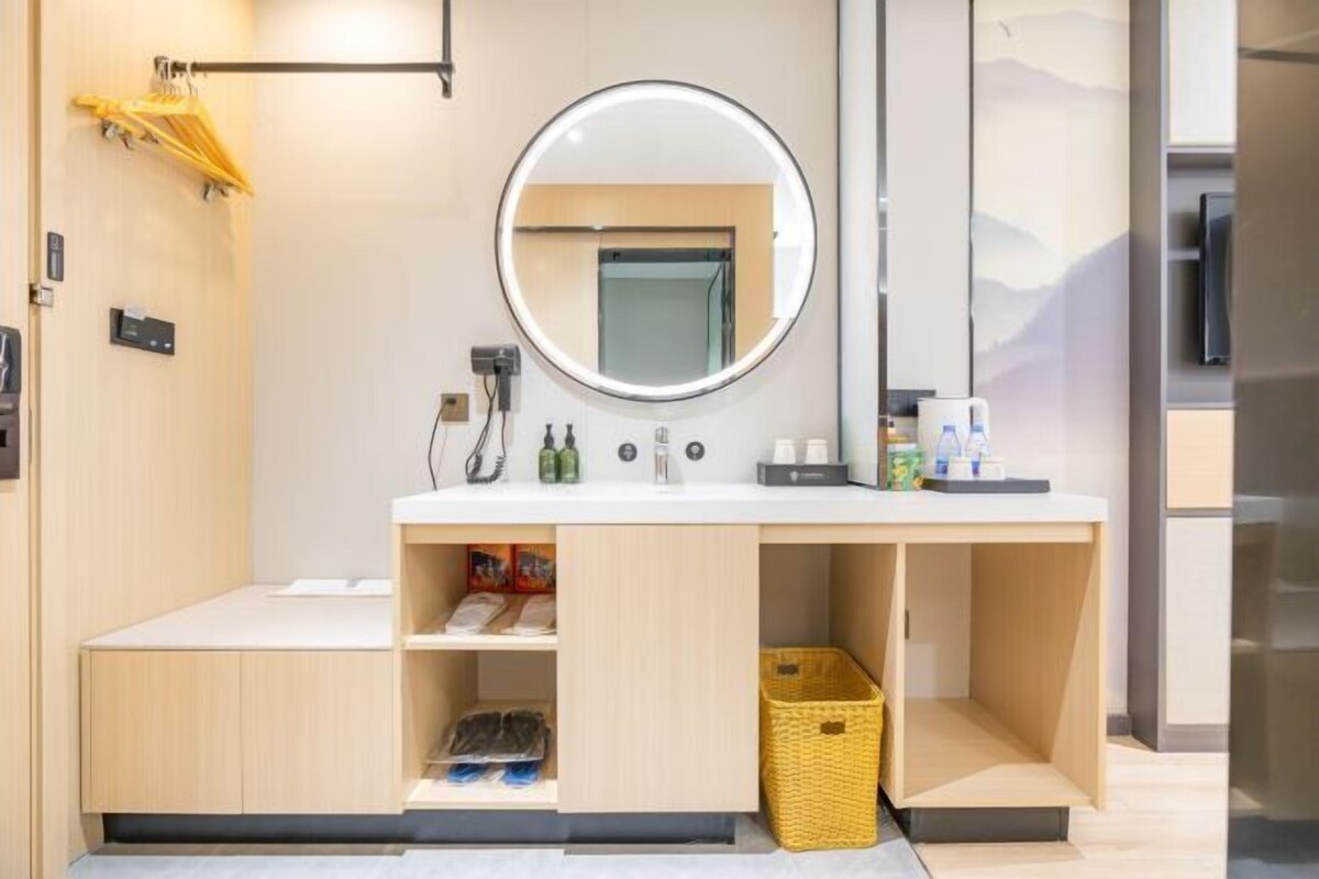 A modern bathroom with a round mirror, white countertop, and wooden cabinets.