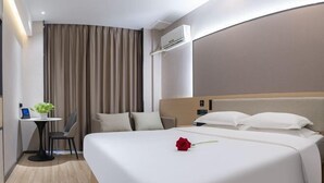 Een hotelkamer met een groot bed, een bureau met stoel, een kleine tafel met plant en een gordijn.