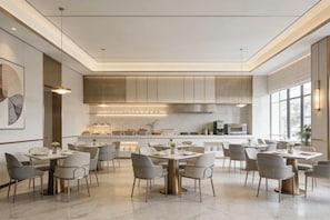 Un comedor moderno con mesas y sillas, una cocina al fondo y un ventanal que proporciona luz natural.