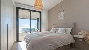 Un dormitorio con una cama grande, vista al mar a través de una puerta corrediza y una lámpara colgante.