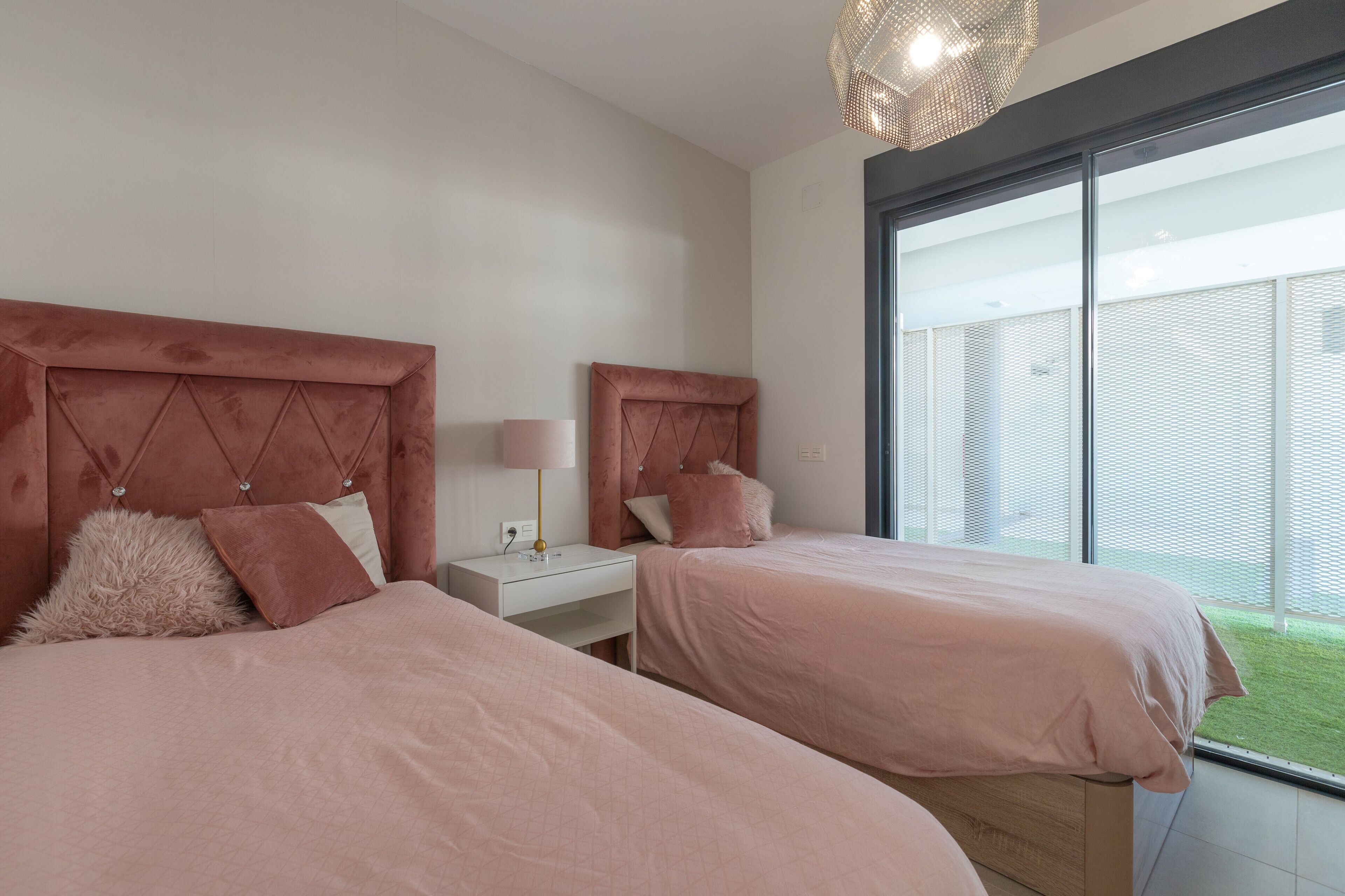 Une chambre avec deux lits, une table de chevet, une lampe et une grande fenêtre donnant sur un espace vert.