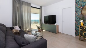 Una sala de estar moderna con un sofá grande, una mesita redonda con una planta, un televisor y vistas al exterior a través de una puerta corredera.