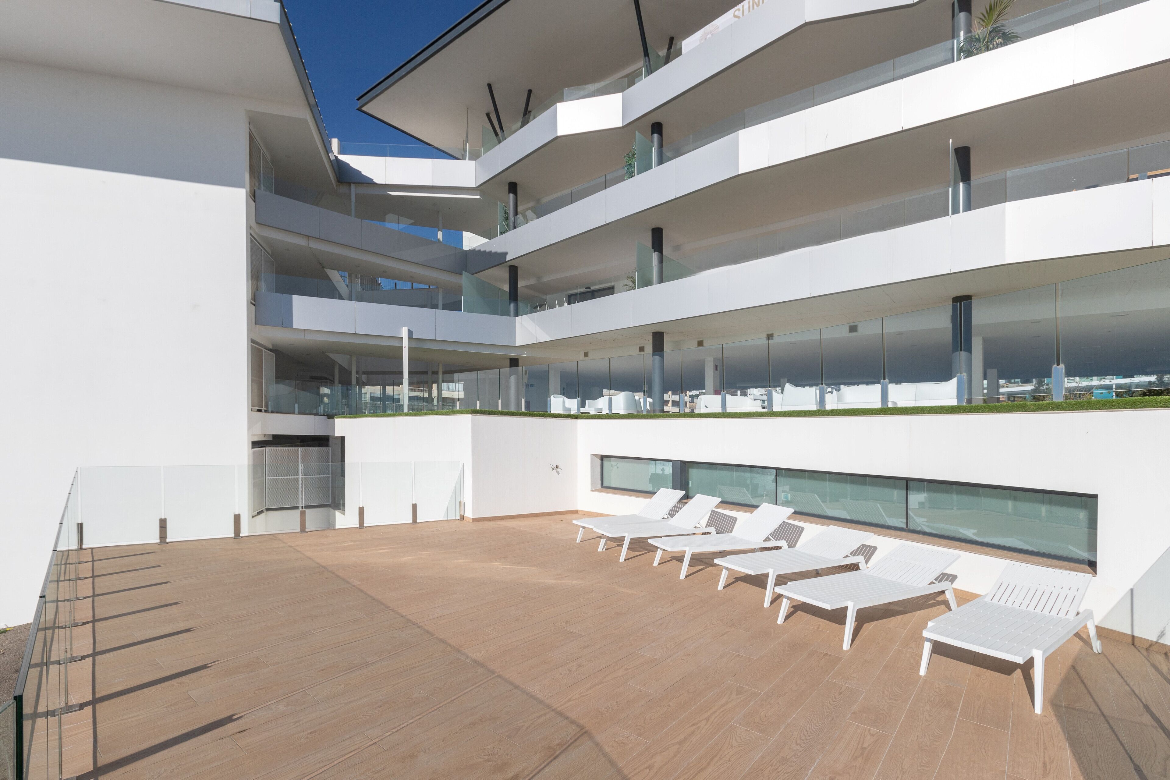 Un bâtiment moderne à plusieurs niveaux, doté d’une terrasse sur le toit aménagée avec des chaises longues et une rambarde en verre.