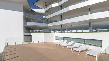 Un bâtiment moderne à plusieurs niveaux, doté d’une terrasse sur le toit aménagée avec des chaises longues et une rambarde en verre.