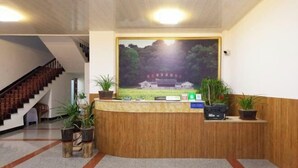 Ein Empfangsbereich mit einem Holzbüro, Topfpflanzen und einem großen gerahmten Bild eines traditionellen Gebäudes.