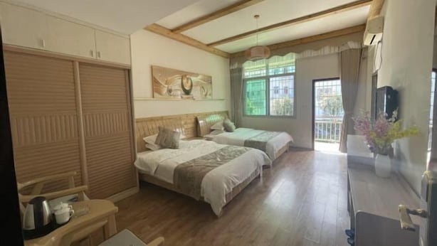 Ein Hotelzimmer mit zwei Betten, Holzboden, einem Fenster mit Vorhängen, einem Fernseher und einem Schreibtisch mit Stuhl.