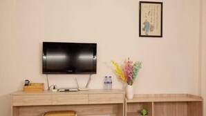 Ein modernes Zimmer mit einem Holztisch, einem Flachbildfernseher, einer Blumenvase und einem gerahmten Kunstwerk an der Wand.