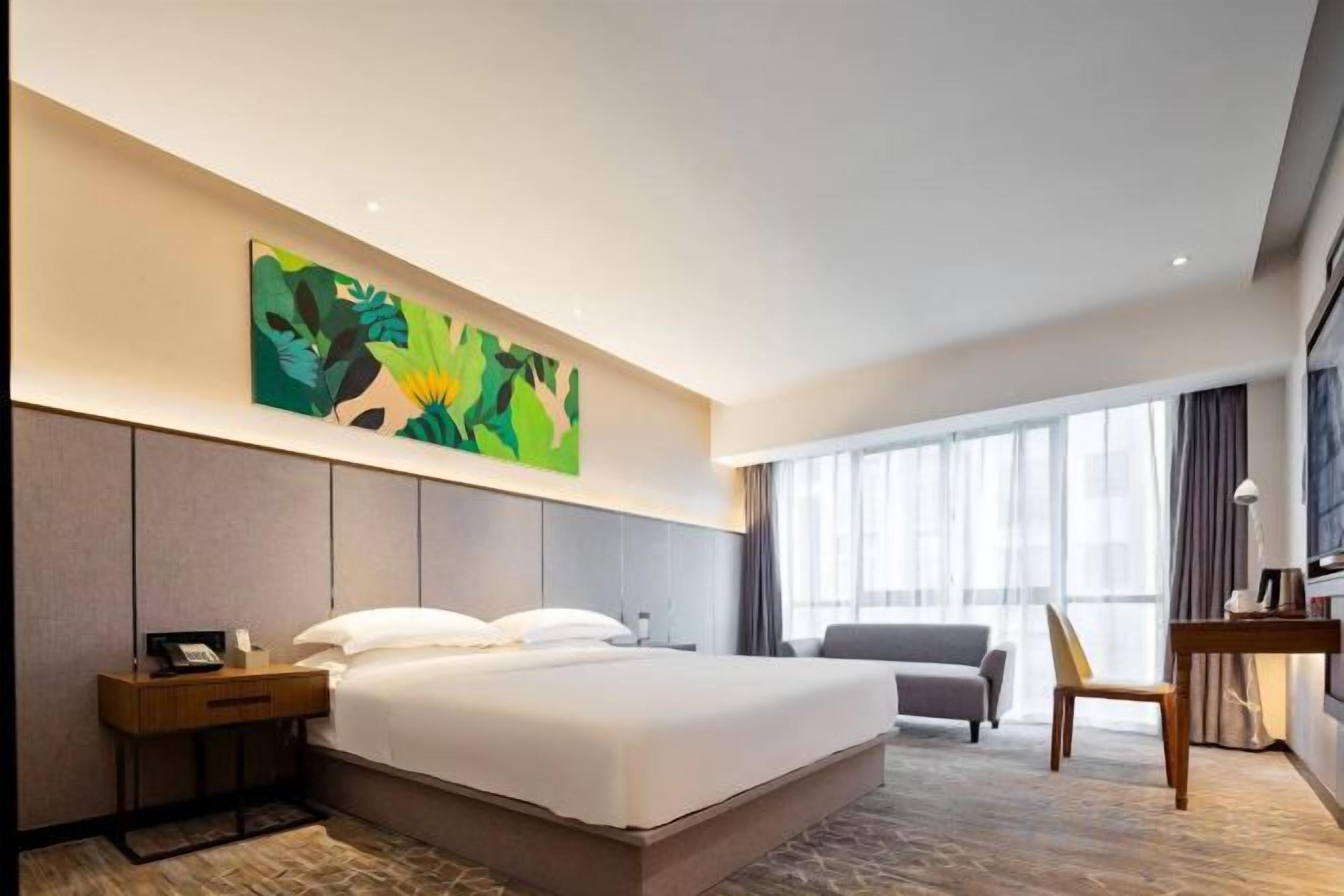A hotel room with a large bed, a desk, a chair, and a painting on the wall.