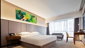 Una habitación de hotel moderna con una cama grande, un escritorio, una silla y un ventanal con cortinas.