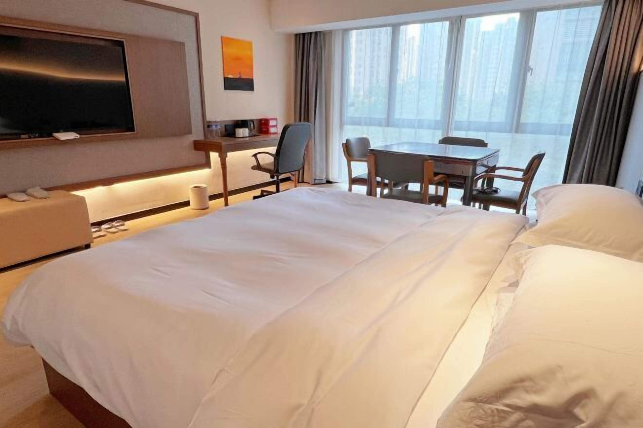 A hotel room with a large bed, a desk with a chair, a TV, and a window with curtains.