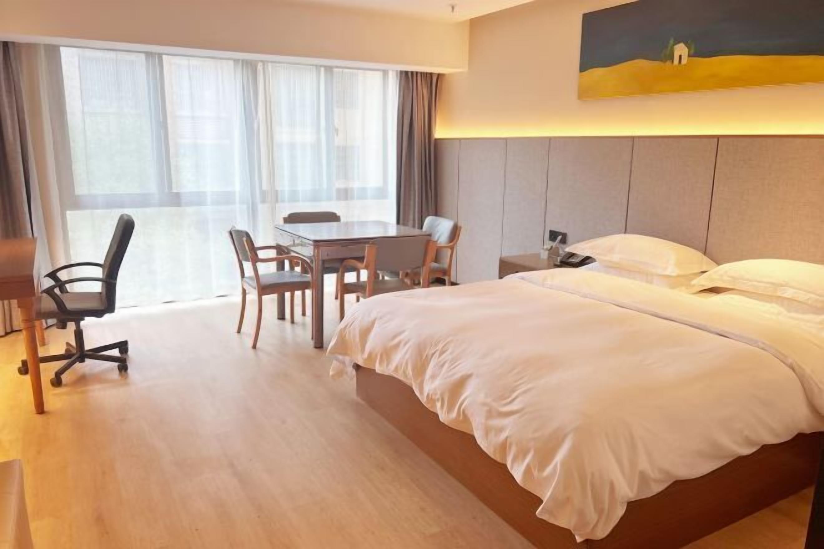 A hotel room with a large bed, a desk with two chairs, a small table, and a painting on the wall.