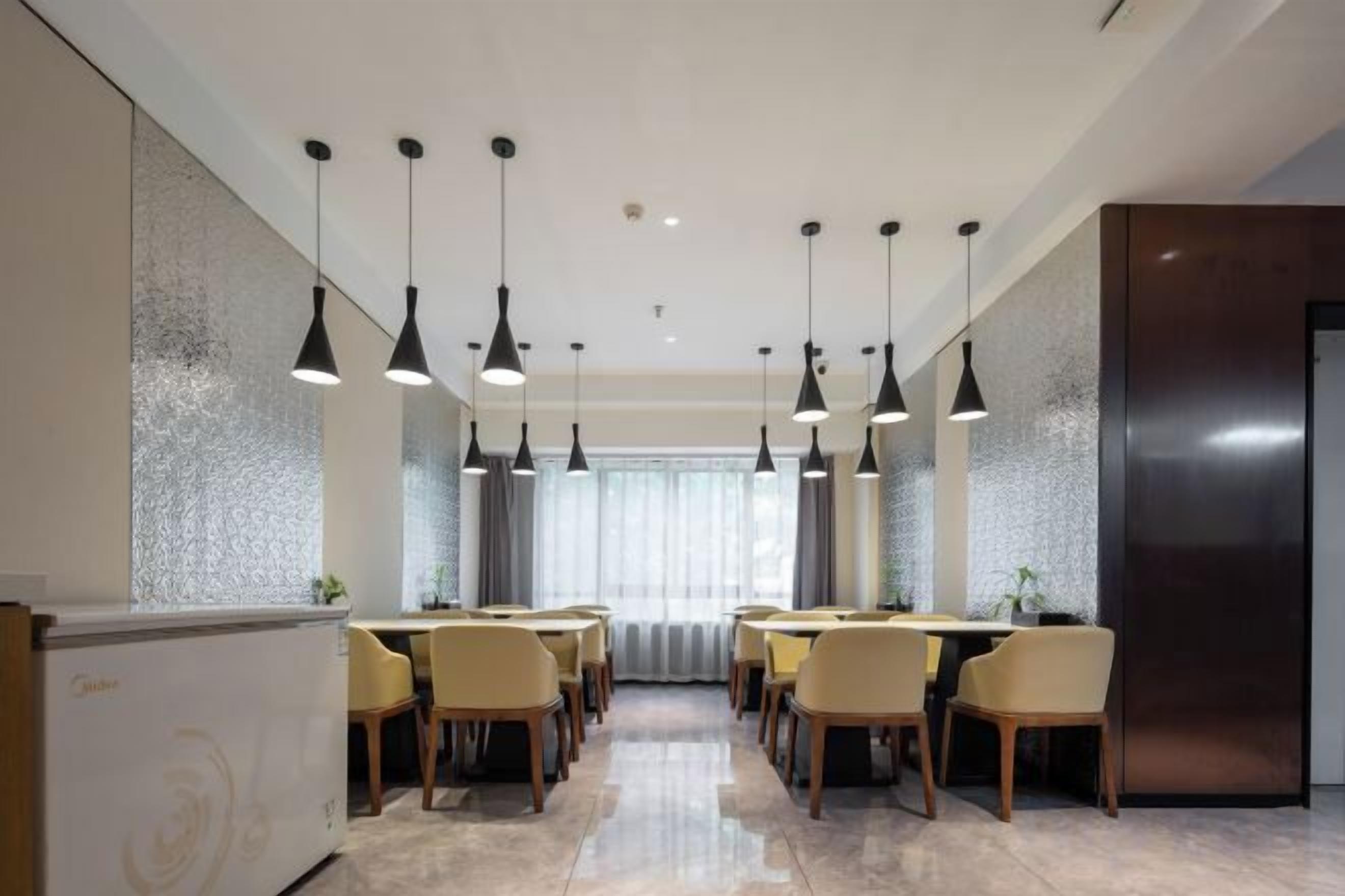 A modern dining area with multiple tables and chairs, pendant lighting, and a large window with curtains.