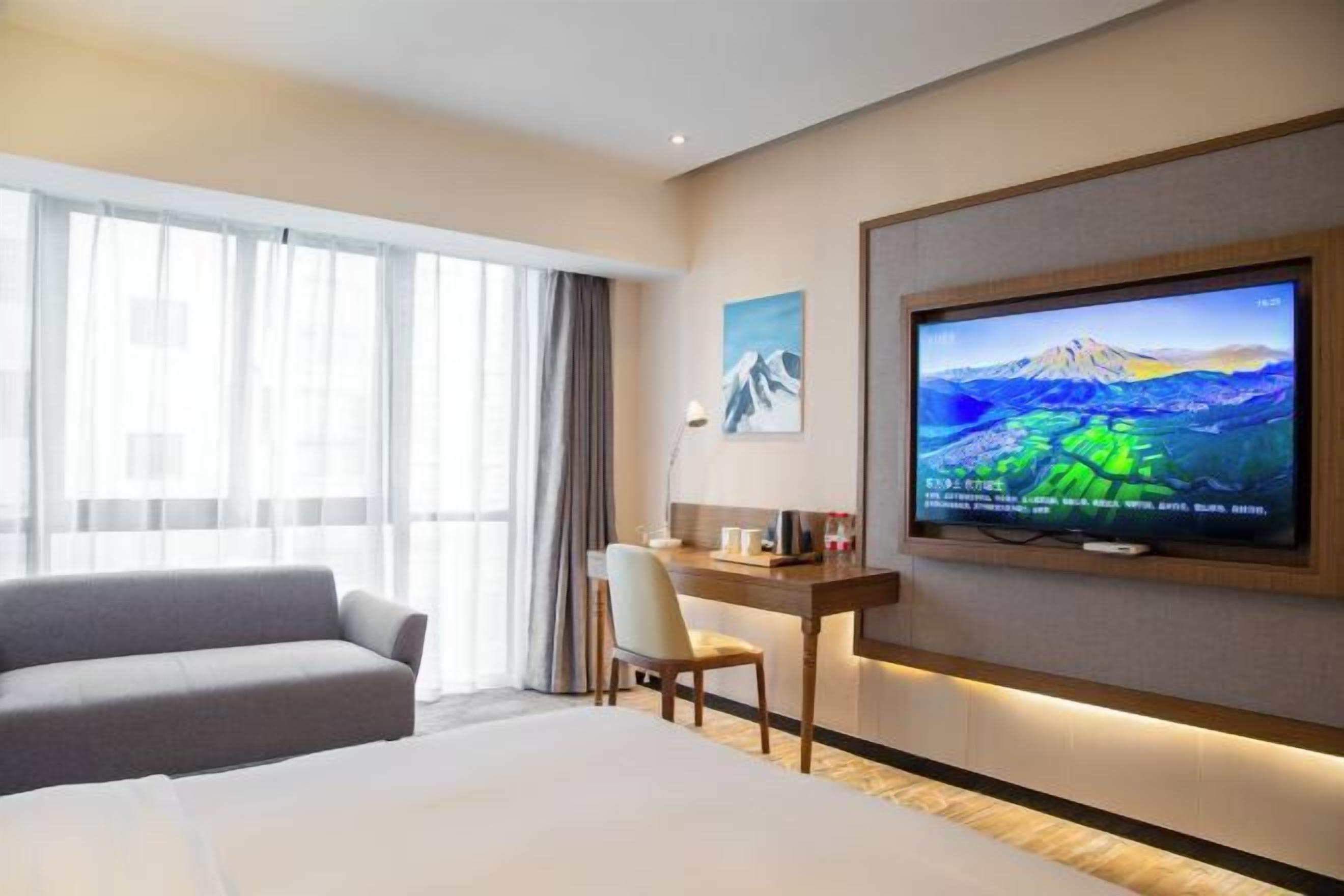 Een hotelkamer met een bed, een bureau, een stoel, een televisie en een raam met gordijnen.