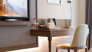 Habitación de hotel con una televisión mostrando una película, un escritorio con una cafetera, una silla y una lámpara.