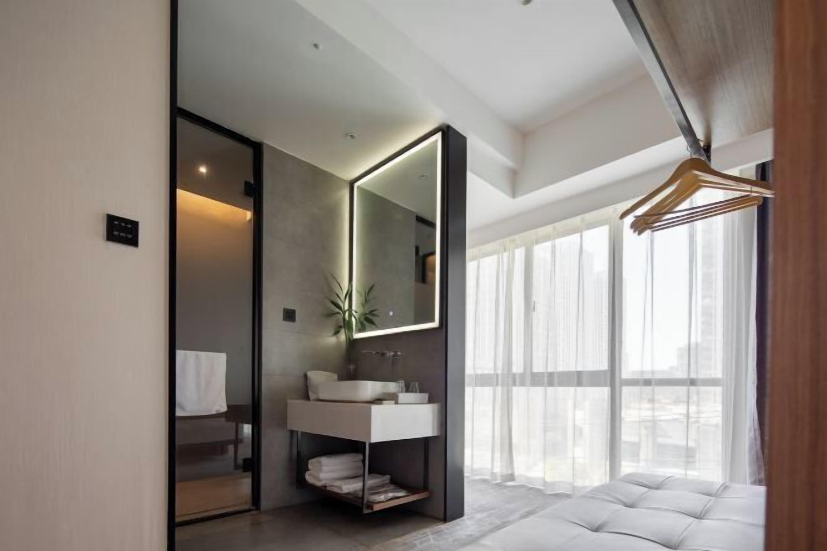 A modern bathroom with a large mirror, a white sink, and a large window with sheer curtains.