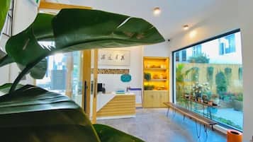 Un interior moderno con una recepción, un banco y vistas a un jardín a través de amplios ventanales.