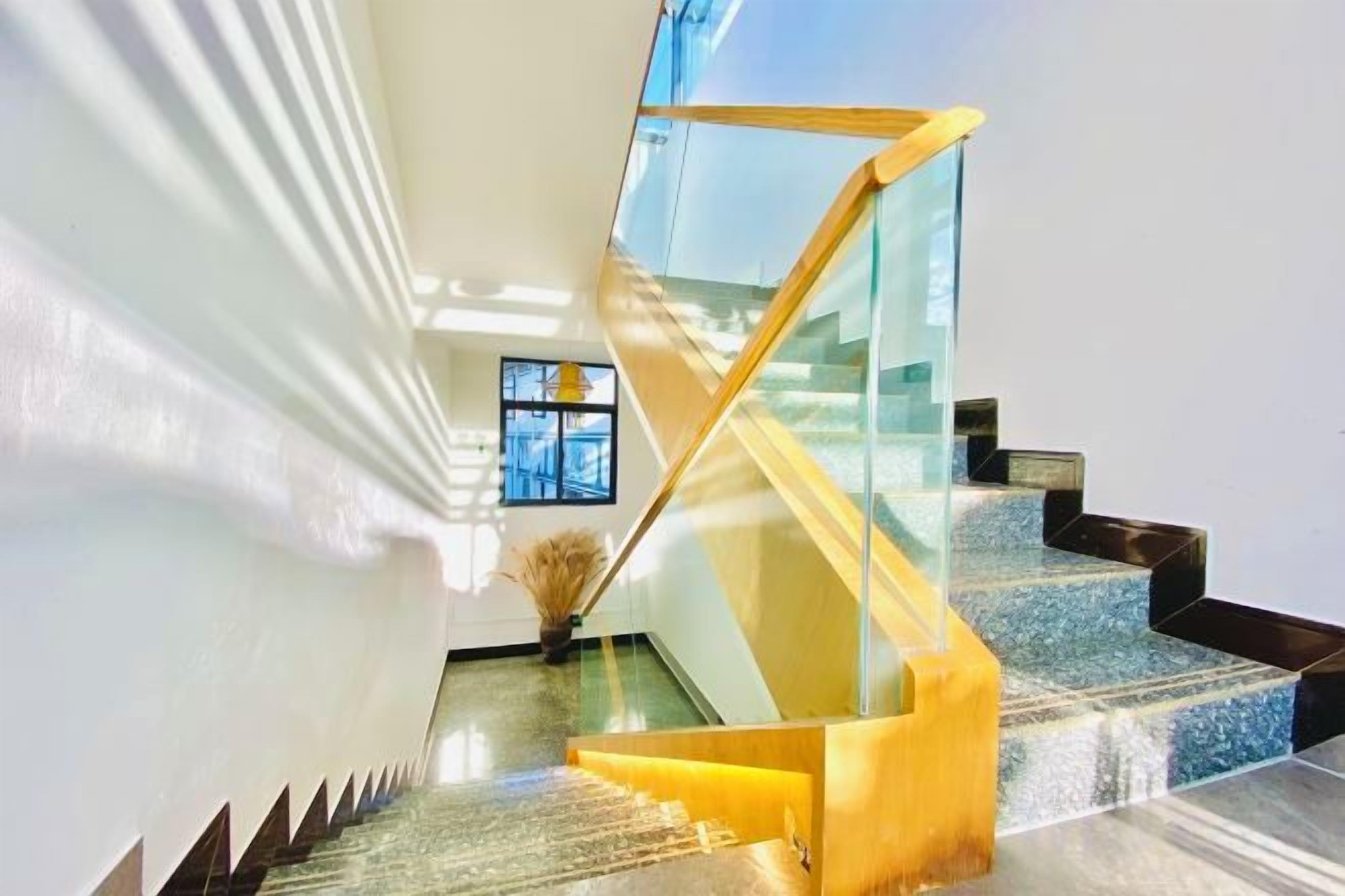 Una escalera moderna con barandillas de vidrio y un pasamanos de madera, que lleva a un piso superior.