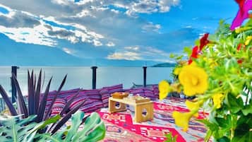 A balcony with a patterned rug, a small wooden table, and a view of the sea.
