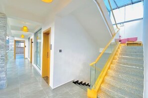 En modern inredning med en spiraltrappa i glas, en hall som leder till ett rum och en utsikt genom ett fönster.