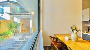 Un comedor con una mesa y sillas de madera, un florero con flores y vistas a un jardín y un edificio.