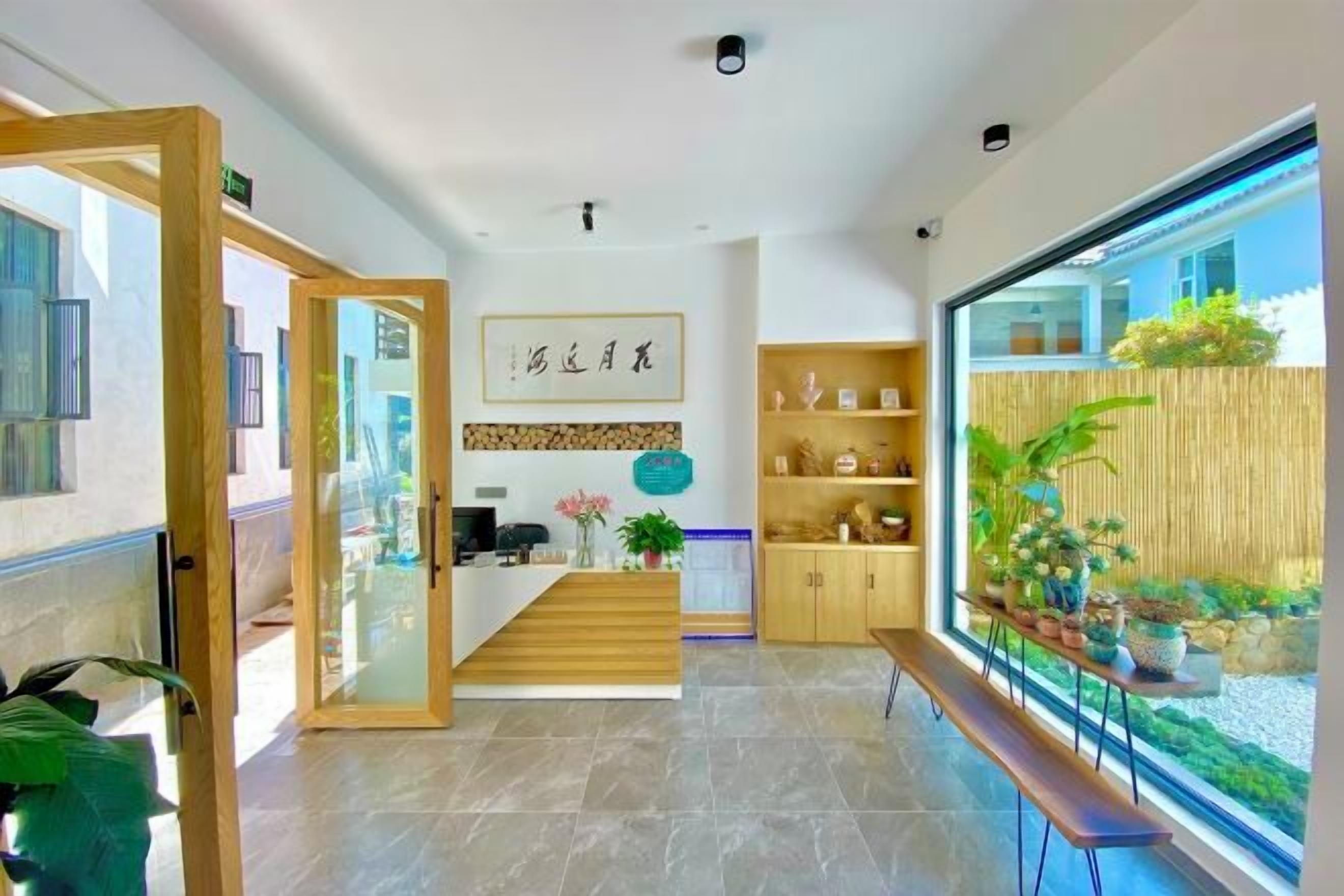 Zona de recepción con un escritorio de madera, mostrador de recepción y vista a un jardín a través de un ventanal grande.